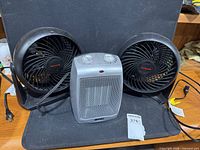 Front view of two Honeywell tabletop fans and one grey ceramic space heater showing overall condition and cords