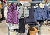All six clothing items hung on rack: purple vest over white shirt, grey vest over black pants, navy garment, denim jacket left to right