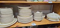 Multiple stacks of Salem Symphony plates, bowls and serving pieces on wooden shelf