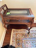 Full view of carved wood tea cart showing glass top, side glass panel, lower shelf, brass casters