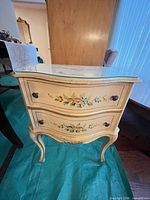 Front view of cream hand-painted floral wood nightstand with glass top and two drawers