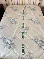 Top view of mattress showing blue floral quilted surface and QUEEN-marked plastic wrap