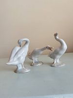 Front view of three cream porcelain geese figurines