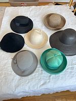 Seven hats laid out showing colours, materials and shapes