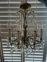Overall view of hanging chandelier showing brass frame, eight candle sockets, crystal prisms