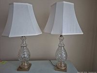 Pair of glass crystal table lamps with white shades on brass bases