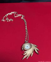 Full view of Lucerna gold-tone pendant watch with chain on red background