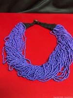 Full view of necklace laid flat showing multiple purple bead strands and black crochet clasp