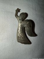Front view of etched brass angel brooch showing engraved motifs and overall shape