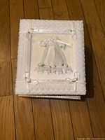 Front cover of white satin baby photo album with lace, bows and rosebud accents