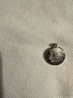 front view of round silver tone locket showing floral engraving and date