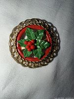 Front view showing gold filigree frame, red ring, green holly leaves, red berries