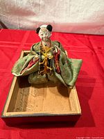Front view of seated Hina doll in brocade kimono inside wooden box