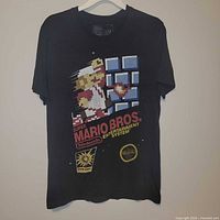 Full front view of black Super Mario Bros graphic t-shirt on hanger