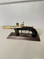 Right side view of brass flintlock pistol on stand