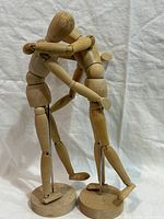 Two wooden mannequins posed hugging on bases