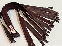 Bundle of ten dark brown zippers laid out, overall view