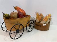 wooden wagon filled with assorted faux produce beside wood bin of corn