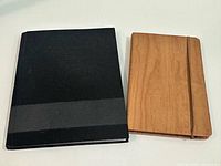 Front covers of black hardcover notebook and wood veneer journal