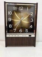Front view of Bulova transistor clock showing dial, numerals, hands, lower speaker grill and strike switch.