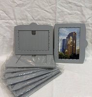 Front and back views of gray plastic photo frames with cityscape image plus sealed stack