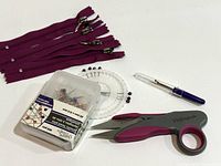 Overview showing four purple zippers, pin wheel, boxed pins, seam ripper, snips