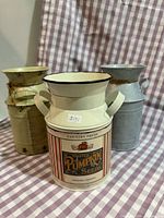 Front view of three metal milk cans showing colors and label