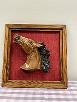 Frontal view of framed ceramic horse head on red fabric