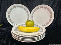 Stack of white plates with geometric border, fruit for scale