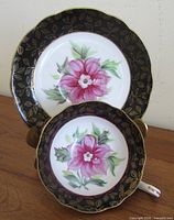 Teacup saucer front and rear view showing orchid design and black-with-gold leaf border