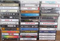 Three vertical stacks showing cassette spines with titles and artists, evidencing quantity and variety