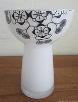 Front view of white glass candle holder showing black geometric motif and pedestal shape