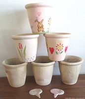 stacked view of six blush pink terracotta pots and two ceramic herb markers