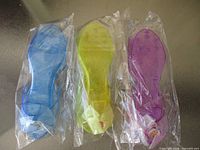 Three sealed pairs of blue, yellow-green, purple plastic dress-up shoes