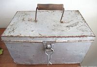 Closed aluminum box, handle up, front view showing latch