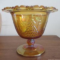 Side view of marigold carnival glass compote showing grape pattern and pedestal
