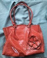 Front view of red crocodile-embossed faux leather shoulder bag, showing flower appliqué and straps