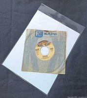Front view of 7" single in Kapp Records sleeve inside clear poly outer sleeve