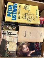 Top view showing Peter Ustinov novel, three paperbacks beneath, partial red spine book