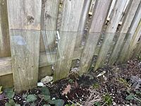 Rectangular clear glass panel leaning against wooden fence