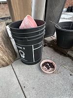 Black nursery bucket with pink ceramic pot inside, adjacent black planter and small pink bowl-pot
