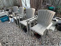 Four light gray resin patio armchairs lined up on gravel