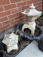 Both resin pagoda lanterns positioned in planters beside brick wall