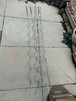 Five wavy metal garden stakes laid on paving for scale