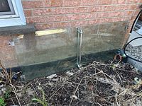 Two clear glass panels leaning against brick wall, showing size and condition, with stainless brackets attached
