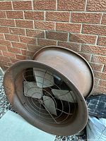 Full view of rusted cast iron fan body leaning against brick wall