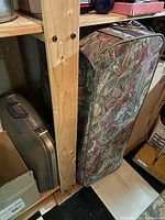 Soft-sided tapestry suitcase next to metal suitcase on shelf