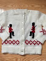 Full front view of white hand-knit cardigan with toy soldier motifs and buttons