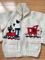 Full view of off-white handknit zip sweater showing train motifs and shawl collar
