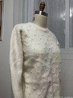 Front and partial side view of off-white sweater on dress form showing pearl embellishments and overall condition
